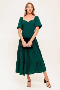 Woman wearing a green dress holding a black clutch against a white background