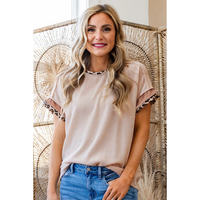 Woman wearing a beige blouse with lace trim and blue jeans, sitting on a woven chair.