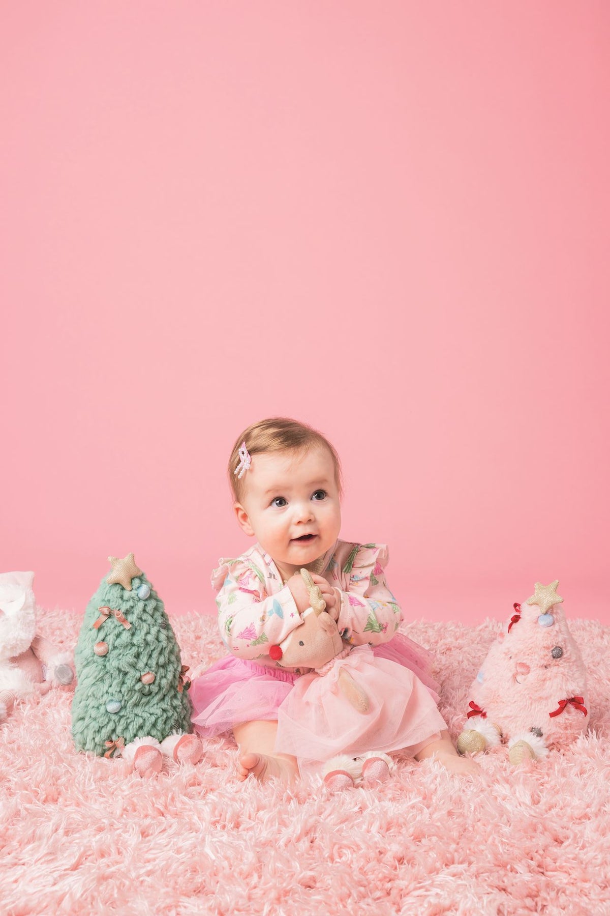 Baby sitting beside Mud Pie sage green Christmas tree plush with weighted seat