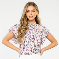 Woman wearing a patterned blouse and white shorts on a plain background