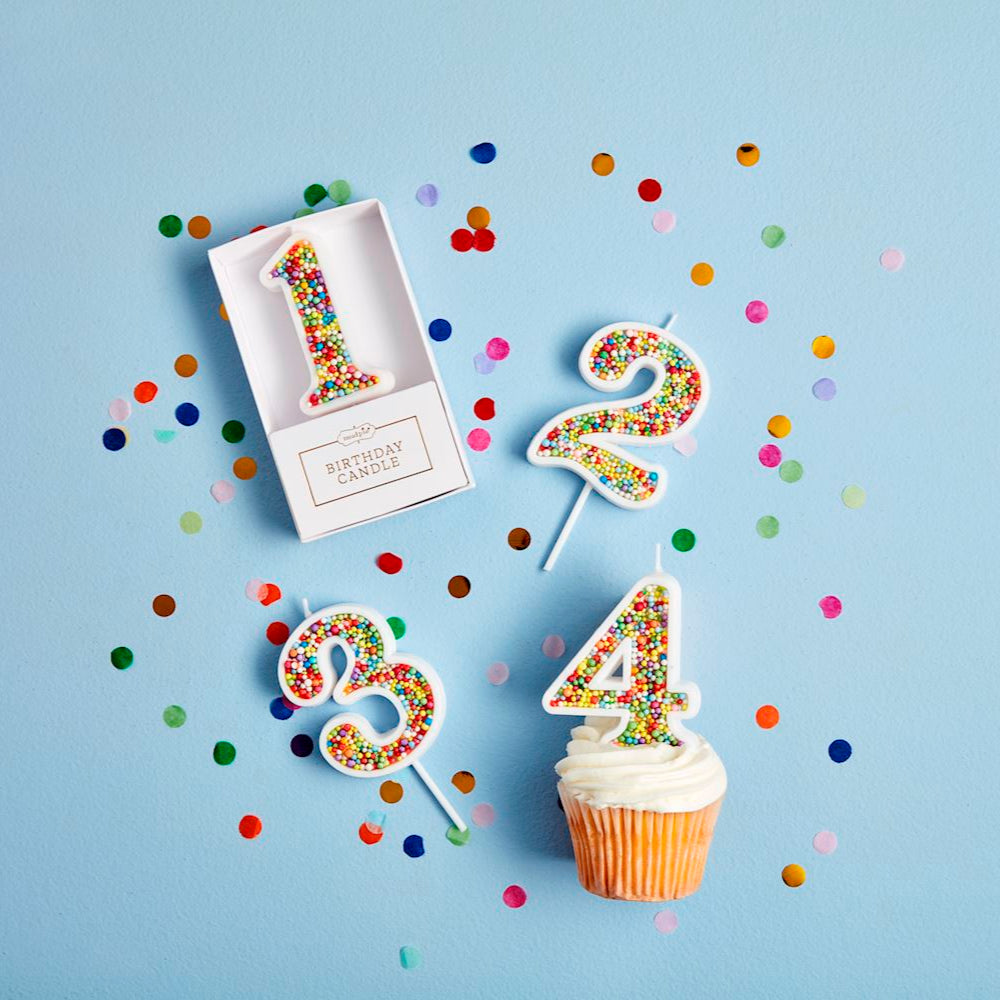 Colorful number candles on a cupcake with confetti against a light blue background