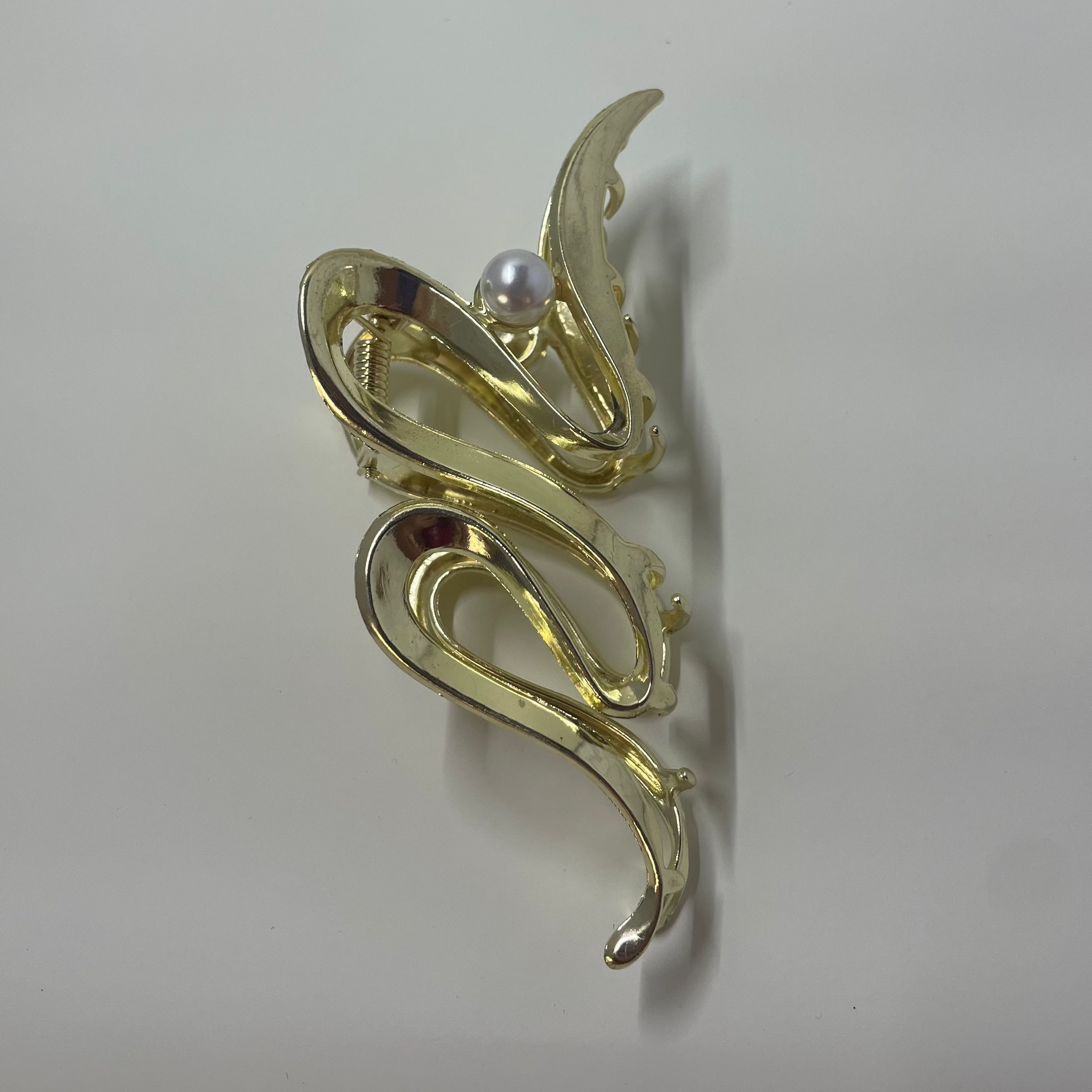 Gold ribbon shaped hair clip with a pearl on a white background