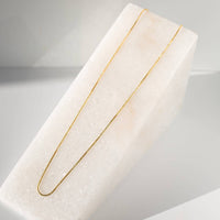 Gold necklace on a white marble stand with a neutral background