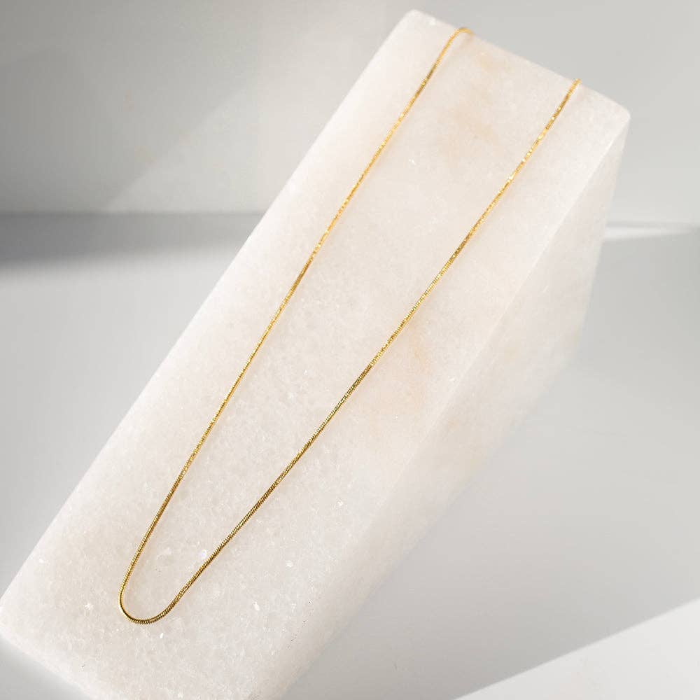 Gold necklace on a white marble stand with a neutral background