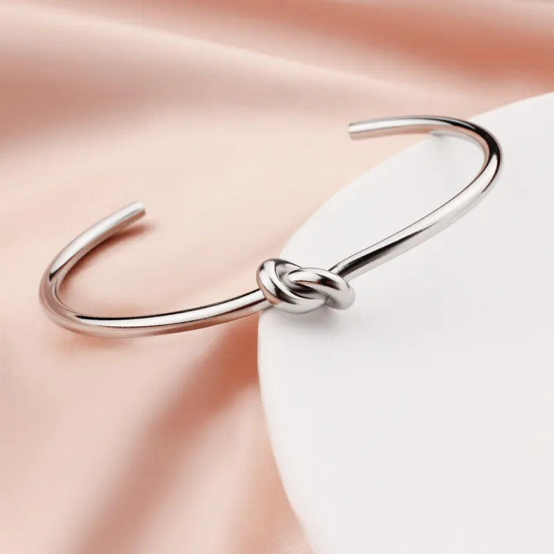 Silver mirror-polished stainless steel C-shaped open cuff bangle with a heart knot design