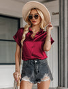 Woman wearing a red blouse, denim shorts, and a beige hat outdoors.