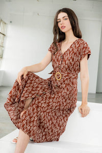 Woman wearing a brown patterned dress sitting on a white surface.