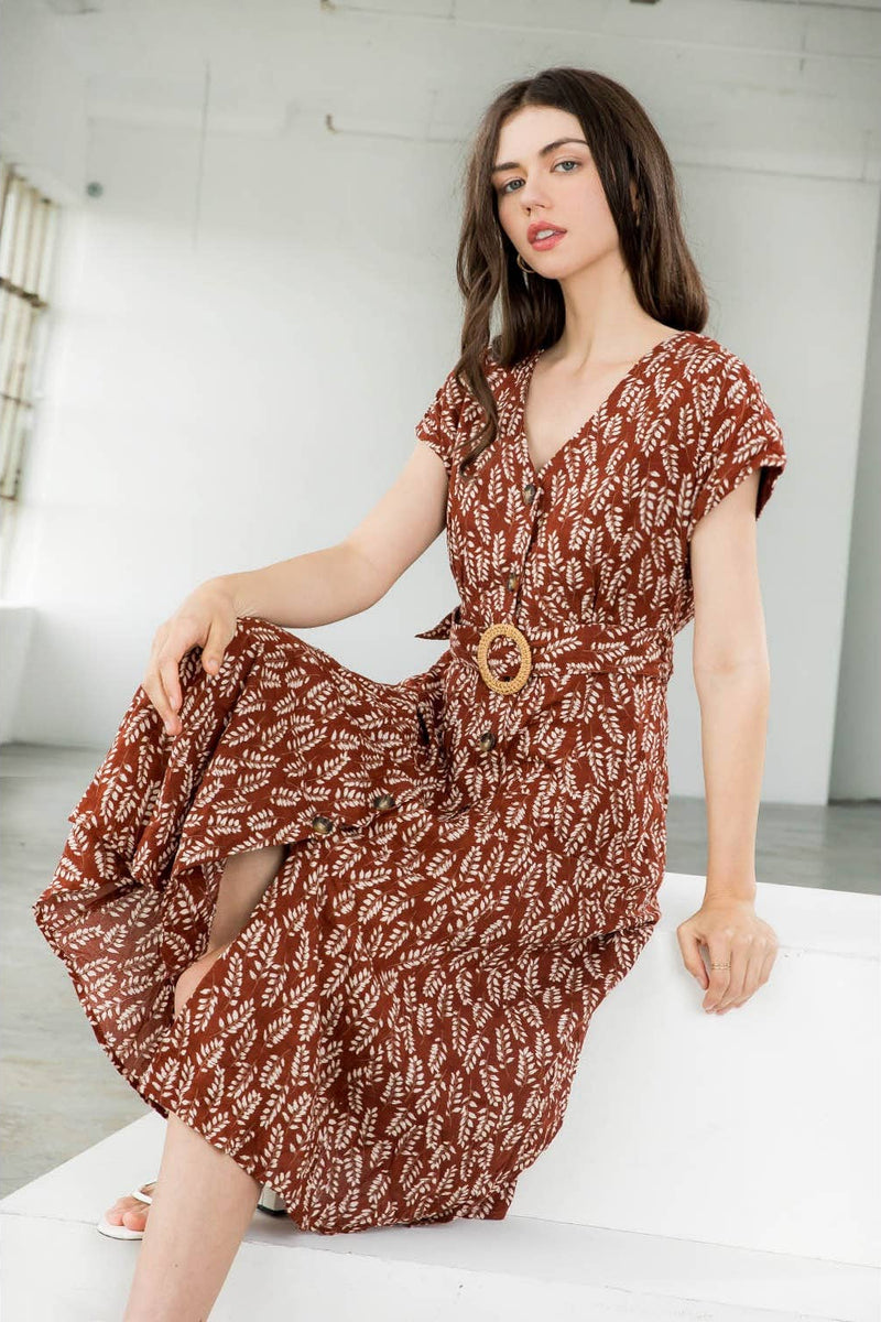 Woman wearing a brown patterned dress sitting on a white surface.