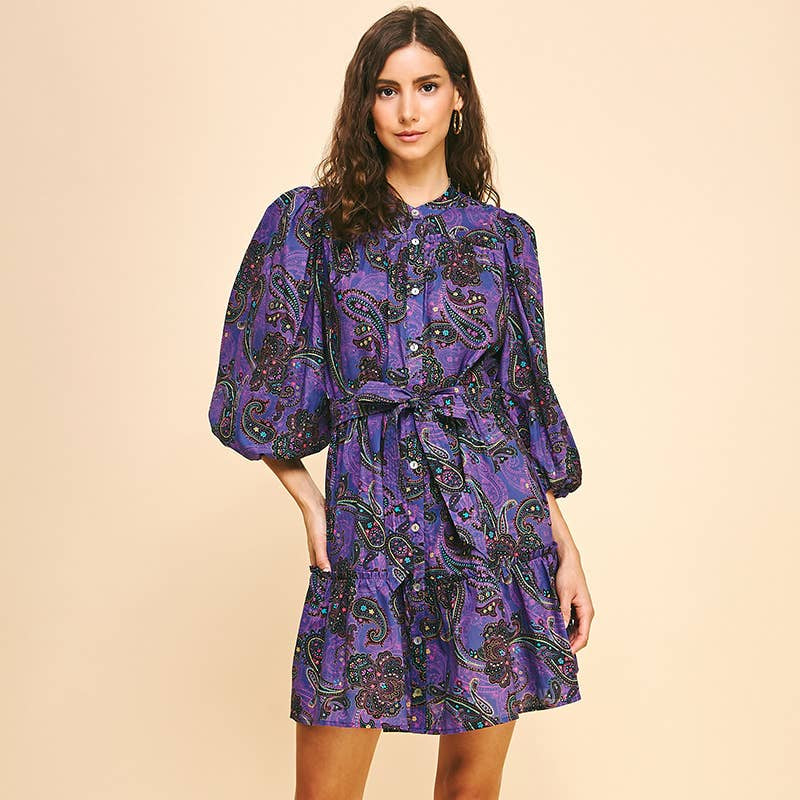 Woman wearing a purple patterned dress with black boots on a beige background