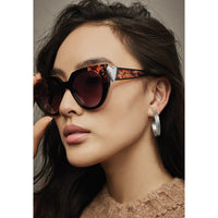 Model wearing Brighton tortoiseshell cat-eye sunglasses with silver heart accents