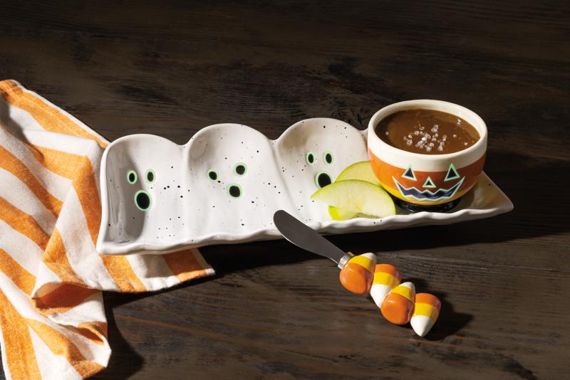 Halloween-themed ceramic ghost plate with a bowl of soup and candy corn on a wooden surface.